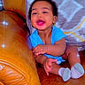 Kyaire is registered to the contest to win money with this photo: baby, child, blue_onesie, leather_couch, smiling, happy, indoors, blanket, socks, sparkles, face, person, seated, cute, home, cozy, infant, plush, furniture, portrait