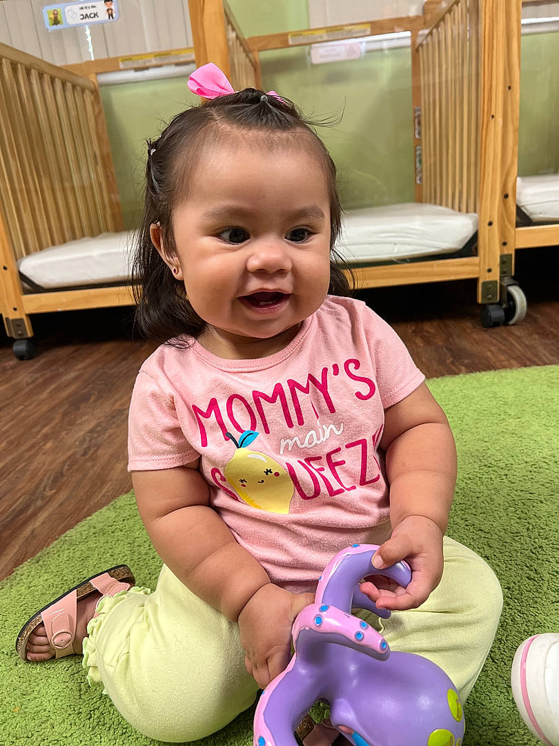 Allyson is registered to the contest to win money with this photo: baby, baby_toddler_clothing, cheek, child, flooring, fun, grass, green, happy, leisure, magenta, mammal, person, pink, play, sitting, skin, smile, snapshot, toddler