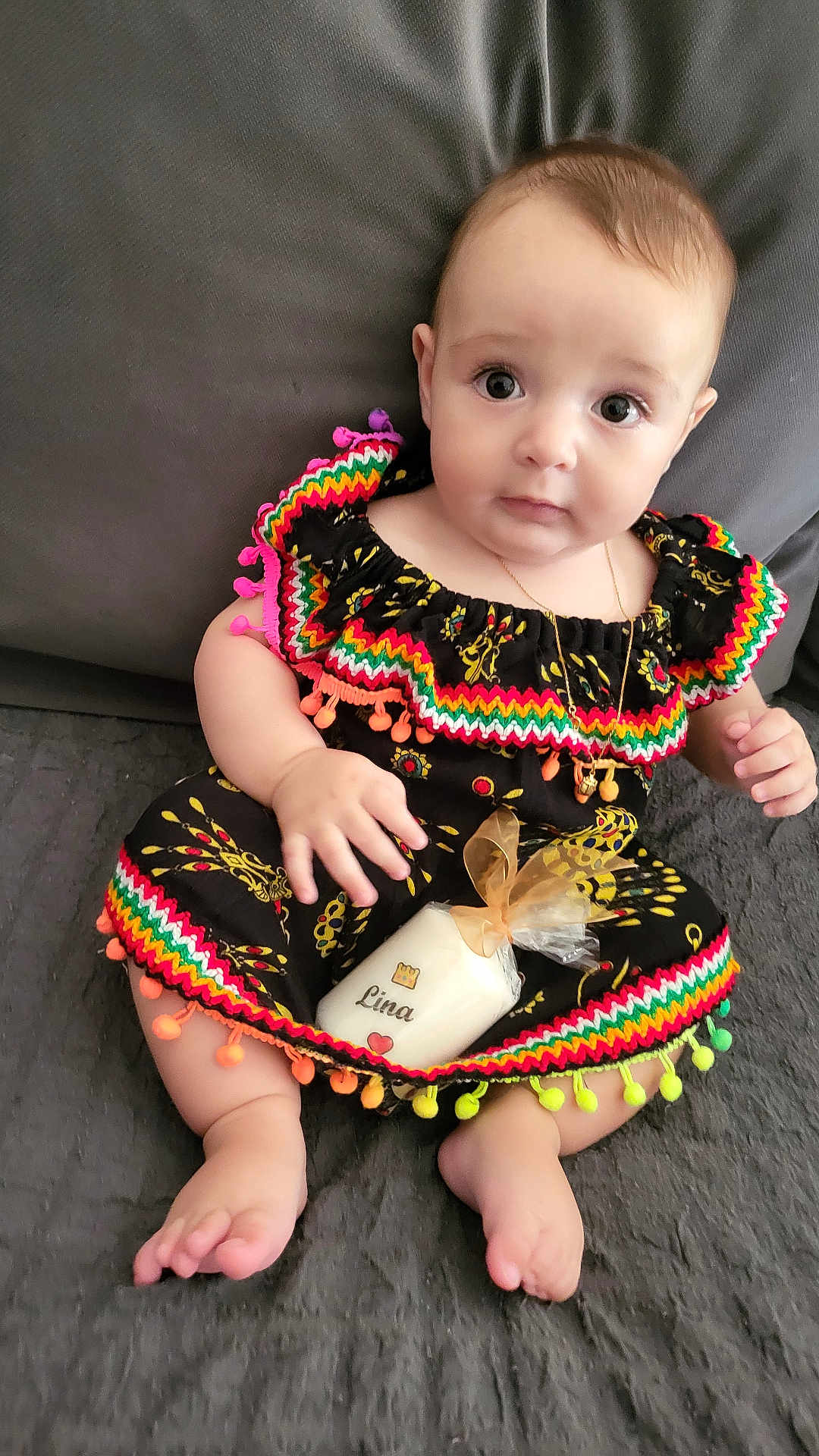 Lina a rejoint le concours — aidez-le/la à gagner de superbes lots ! baby, infant, dress, colorful_clothing, pom_poms, candle, wrapped_gift, sitting, gray_background, cute, child, portrait, indoors, jewelry, necklace, footwearless, hand, face, eyes, soft_surface