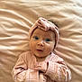 baby, infant, pink_clothing, headband, blue_eyes, lying_down, blanket, cute, portrait, child, soft_texture, newborn, expression, hands, indoor, cozy, small_hands, face, looking_up, adorable