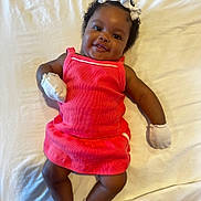 Jream is registered to the contest to win money with this photo: baby, infant, child, smiling, pink_dress, mittens, socks, white_bows, curly_hair, lying_down, white_sheet, happy, cute, portrait, indoors, skin, face, hands, feet, adorable