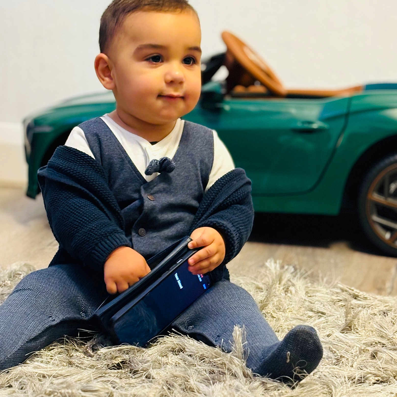 Zayaan joined the competition — help win amazing prizes! car_toy, cardigan, child, clothing, curious, cute, floor, footwear, home, indoor, pants, person, play, portrait, rug, sitting, smartphone, toddler, toy_car, young_child