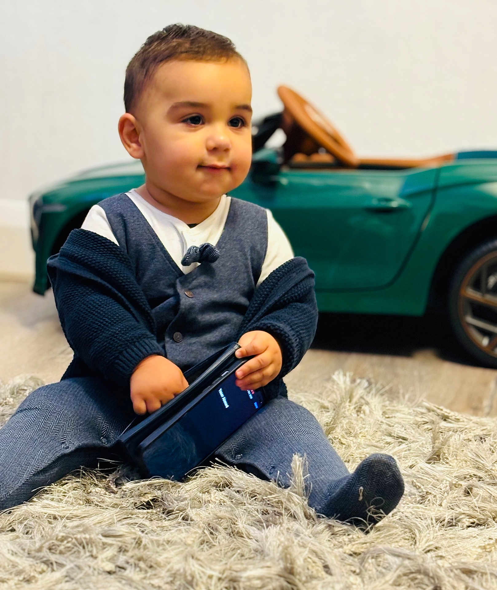 Zayaan joined the competition — help win amazing prizes! toddler, child, indoor, car_toy, rug, smartphone, clothing, sitting, cute, curious, person, footwear, cardigan, pants, toy_car, floor, portrait, young_child, home, play