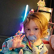 Saïd participe au concours pour gagner de l'argent avec cette photo : arcade_game, blonde_hair, child, colorful, cozy, curly_hair, cute, face, furniture, hand, indoor, neon_light, pacifier, pajamas, person, playful, reaching, stuffed_animal, toddler, toy