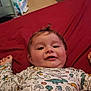 baby, child, infant, dinosaur_print, onesie, red_bedspread, smiling, lying_down, cute, happy, indoors, portrait, young_child, toddler, clothing, head, face, sleepwear, playful, cozy