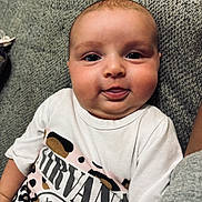 Elodie joined the competition — help win amazing prizes! baby, infant, face, tongue, expression, nirvana_shirt, clothing, couch, gray, texture, skin, person, cute, chubby, head, eyes, indoor, comfortable, young_child, happy