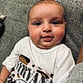baby, infant, face, tongue, expression, nirvana_shirt, clothing, couch, gray, texture, skin, person, cute, chubby, head, eyes, indoor, comfortable, young_child, happy
