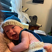 Bobby is registered to the contest to win money with this photo: arm, baby, cat_scratch_post, child, closeup, cozy, curtains, fabric, face, furniture, happy, indoor, knitted_hat, knitted_outfit, person, resting, skin, smiling, window, wood