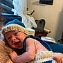 arm, baby, cat_scratch_post, child, closeup, cozy, curtains, fabric, face, furniture, happy, indoor, knitted_hat, knitted_outfit, person, resting, skin, smiling, window, wood