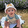 baby, child, hat, striped_hat, lion_patch, outdoor, grass, flowers, purple_flowers, blue_eyes, curious, sitting, cloth, sunlight, nature, cute, infant, smiling, barefoot, young_child