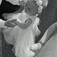 Kaïna participe au concours pour gagner de l'argent avec cette photo : toddler, child, dress, flower_crown, hands, adult, tattoo, bracelet, outdoor, pavement, black_and_white, smile, lace, celebration, holding_hands, person, cute, happy, baby, family