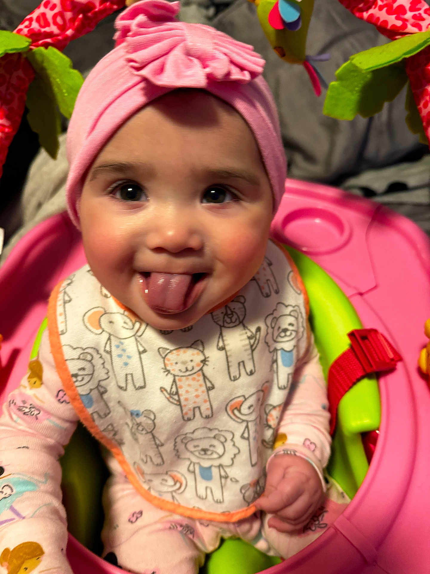Camaria joined the competition — help win amazing prizes! baby, pink_headband, tongue_out, bib, animal_print, pajamas, baby_seat, pink, green, playful, smiling, child, soft_toys, indoors, close_up, cute, infant, face, person, happy