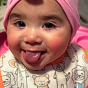 Camaria is registered to the contest to win money with this photo: baby, child, face, tongue, pink_hat, bib, animal_print, cute, smile, rosy_cheeks, playful, closeup, indoors, infant, person, happy, expression, skin, headwear, young