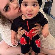 Camaria joined the competition — help win amazing prizes! adult, affection, baby, black_clothing, carpet, casual, child, closeup, cute, family, holding, home, indoor, kiss, love, person, portrait, red_pattern, smile, turban