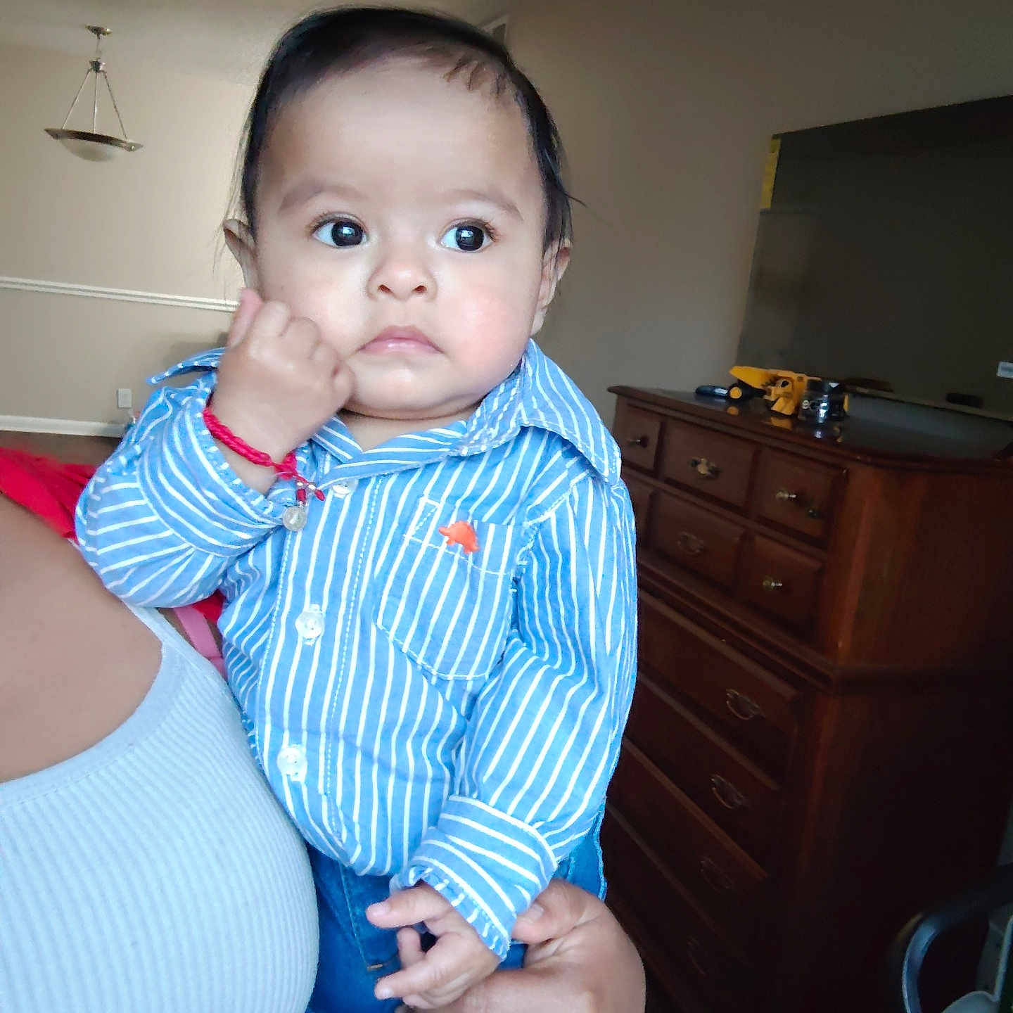 Lyam G Ba Coc is registered to the contest to win money with this photo: baby, blue_clothing, bracelet, casual, child, curious, cute, dresser, expression, furniture, hand, holding, home, indoor, jeans, living_room, person, portrait, striped_shirt, television