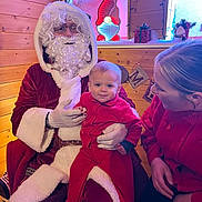 Austin joined the competition — help win amazing prizes! baby, santa_claus, woman, red_clothing, holiday, christmas, wooden_wall, indoor, decorations, lights, gift_box, smile, beard, glasses, face, person, festive, warm_lighting, seated, cozy