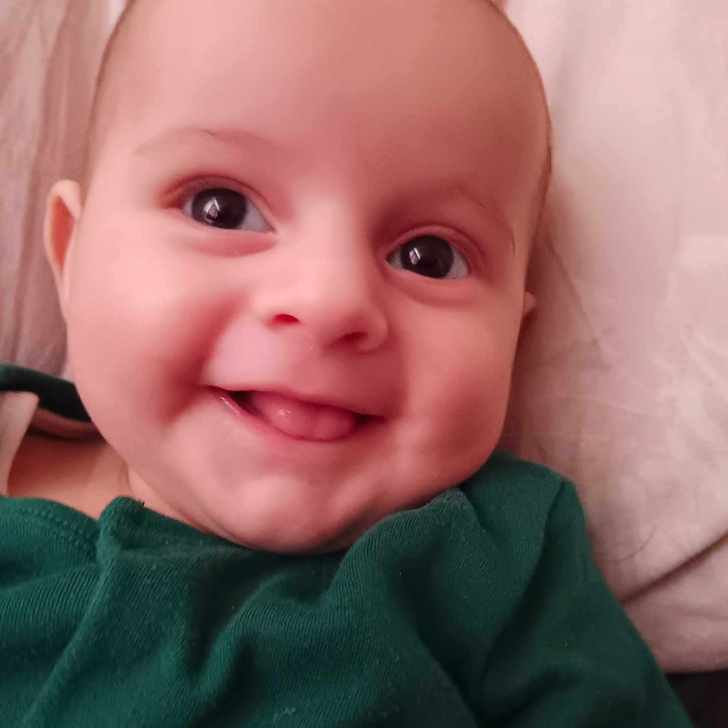 Finlay joined the competition — help win amazing prizes! apparel, baby, child, close_up, cute, expression, eyes, face, green_clothing, head, indoors, infant, lying_down, person, portrait, skin, smiling, soft_lighting, tongue, young