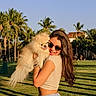 woman, dog, pomeranian, sunglasses, outdoor, park, grass, trees, palm_trees, sunlight, smile, happy, pet, summer, casual_clothing, nature, daytime, portrait, cute, animal