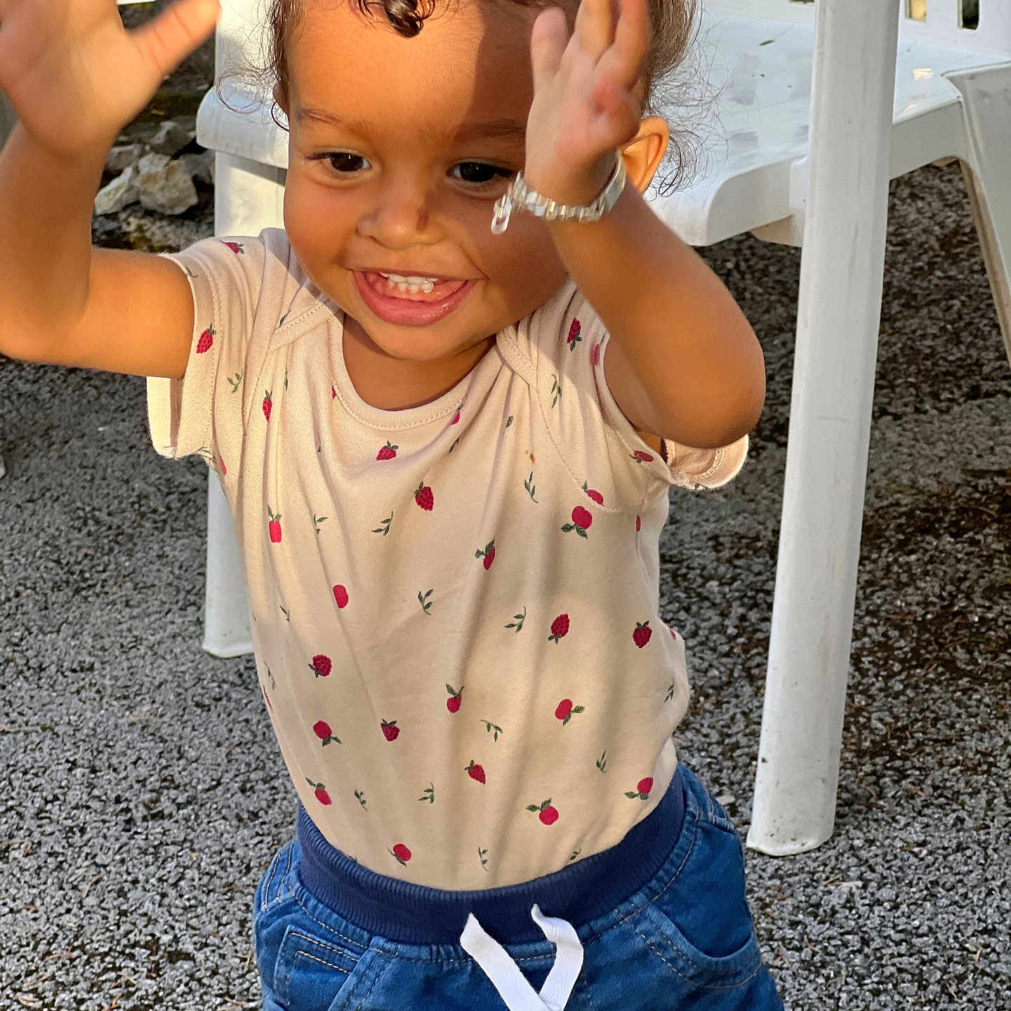 Harena participe au concours pour gagner de l'argent avec cette photo : bracelet, child, clothing, curly_hair, cute, gravel, happy, joy, outdoor, person, pigtails, plastic_chair, playful, portrait, shirt, shorts, smiling, strawberry_pattern, sunlight, toddler
