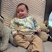 Aaron participe au concours pour gagner de l'argent avec cette photo : baby, infant, smile, pacifier, stuffed_animal, plush_toy, patterned_sweater, beige_pants, socks, chair, cushion, textured_blanket, cozy, portrait, indoor, hand, foot, dark_hair, happy_expression, soft_lighting