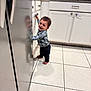 toddler, child, smiling, barefoot, kitchen, cabinet, refrigerator, reflection, tile_floor, plaid_shirt, jeans, person, indoor, home, happy, young_child, curly_hair, standing, domestic, casual_clothing
