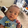 Griffin joined the competition — help win amazing prizes! baby, baby_rocker, blue_onesie, carpet, curtain, expression, face, floor, hair, hand, holding, indoor, infant, light, living_room, person, skin, text_on_clothing, toy, window