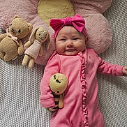 Luna is registered to the contest to win money with this photo: baby, pink, headband, onesie, knit_blanket, plush_flower, knit_toy, knitted_bear, knitted_bunny, smile, cute, infant, toy, soft_toy, cozy, child, lying_down, indoors, happy, portrait