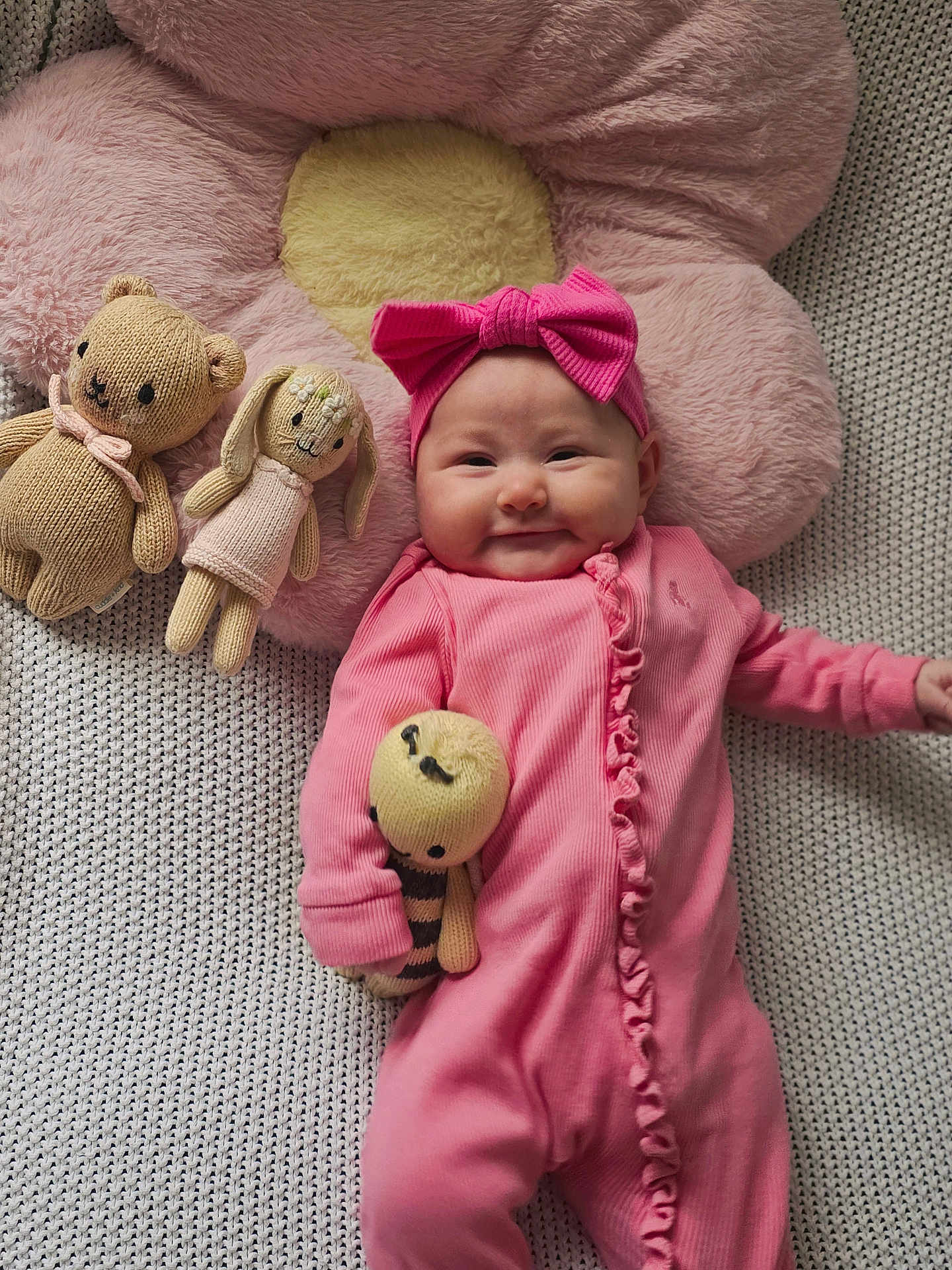 Luna is registered to the contest to win money with this photo: baby, pink, headband, onesie, knit_blanket, plush_flower, knit_toy, knitted_bear, knitted_bunny, smile, cute, infant, toy, soft_toy, cozy, child, lying_down, indoors, happy, portrait