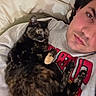 person, cat, tortoiseshell_cat, indoor, couch, blanket, casual_clothing, face, pet, relaxing, cozy, resting, curious, closeup, human_animal_interaction, home, comfort, fur, portrait, laying_down