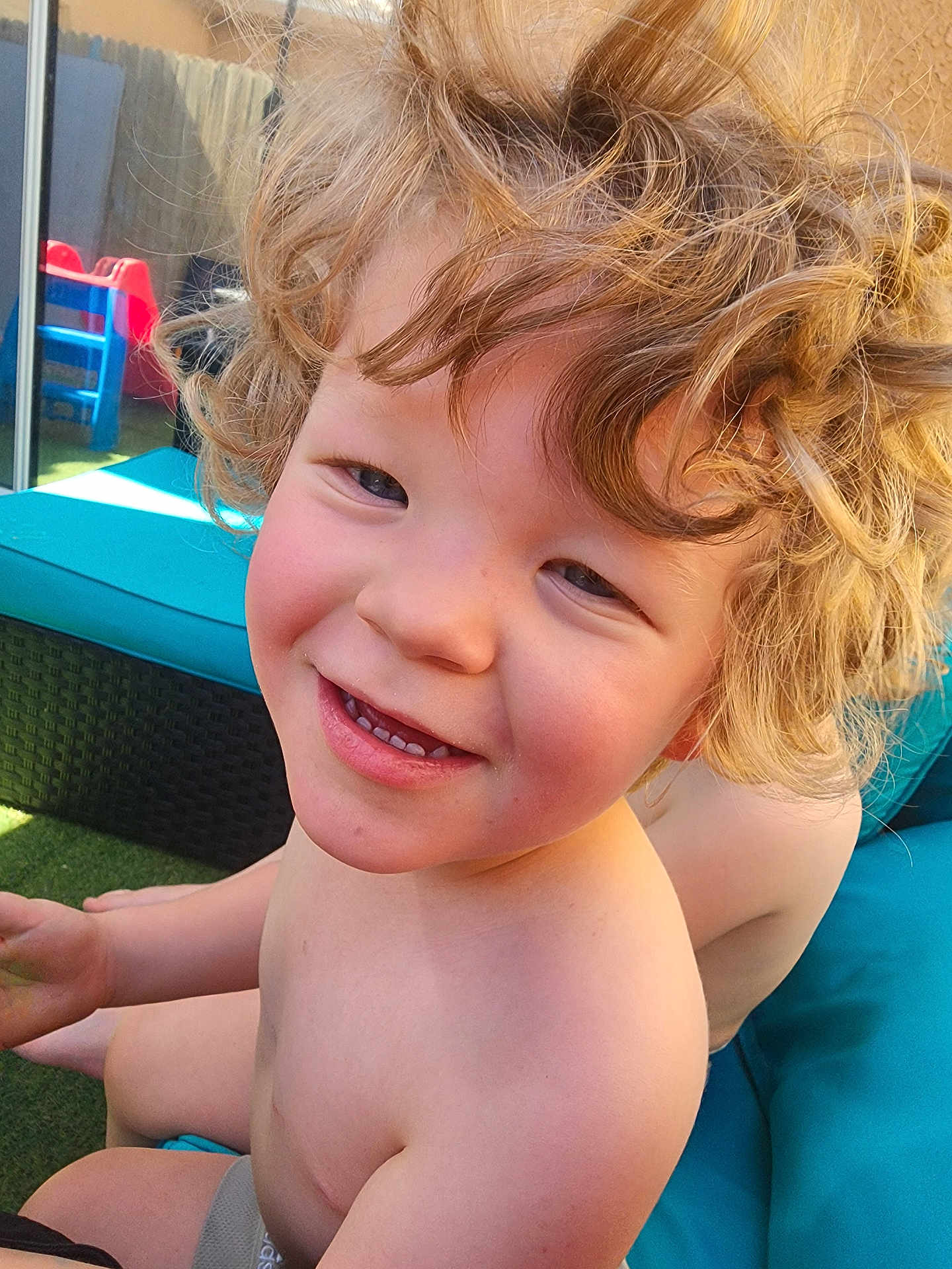 Jared Blodgett is registered to the contest to win money with this photo: child, smiling, blonde_hair, curly_hair, outdoor, sunlight, play_area, plastic_chair, cushion, bare_chest, happy, closeup, person, grass, furniture, daylight, skin, young, portrait, play
