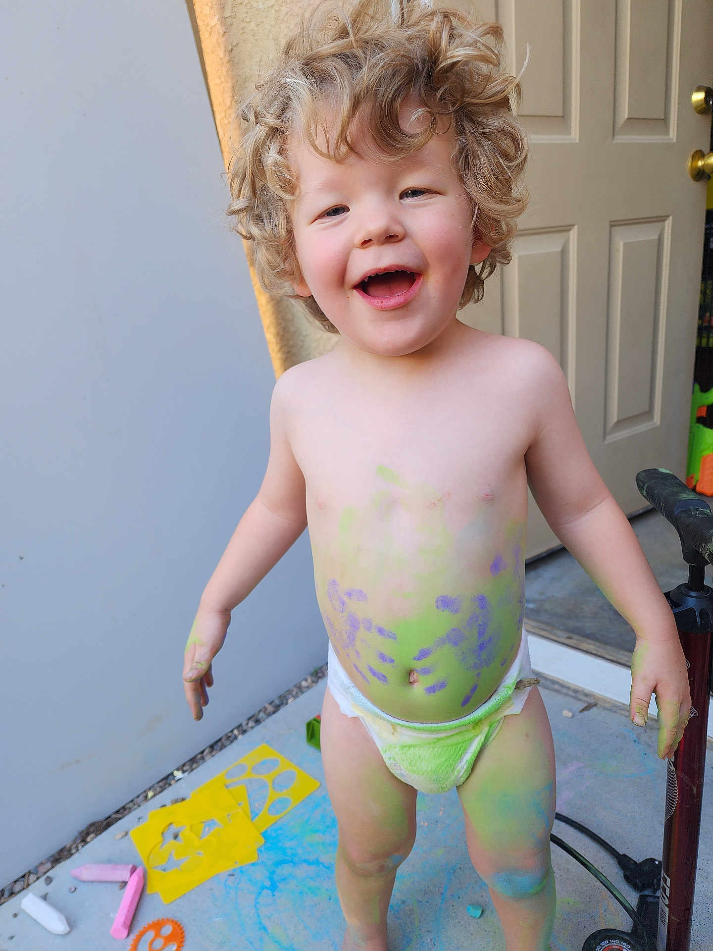 Jayden Blodgett joined the competition — help win amazing prizes! toddler, child, curly_hair, diaper, chalk_paint, colorful, smiling, outdoor, concrete_floor, stencils, chalk, playful, happy, bare_chest, feet, door, pump, hand_painted, messy, fun