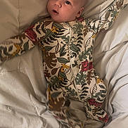 Liam joined the competition — help win amazing prizes! baby, infant, onesie, blanket, sleepwear, cute, child, lying_down, patterned_clothing, animal_print, leaves, soft_texture, indoors, bed, portrait, young_child, small_arms, curious_expression, head, face