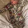 baby, infant, onesie, blanket, sleepwear, cute, child, lying_down, patterned_clothing, animal_print, leaves, soft_texture, indoors, bed, portrait, young_child, small_arms, curious_expression, head, face