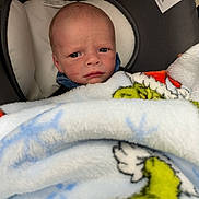 Adam joined the competition — help win amazing prizes! baby, infant, car_seat, blanket, cartoon_character, face, expression, serious, indoor, child, cushion, fabric, clothing, seatbelt_warning, person, portrait, newborn, soft_texture, closeup, wrapped