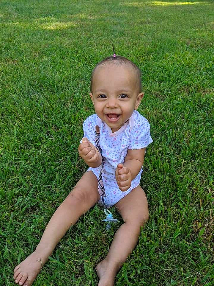 Sunnie is registered to the contest to win money with this photo: baby, baby_toddler_clothing, barefoot, child, finger, fun, grass, grass_family, green, happy, head, lawn, leg, meadow, person, plant, sitting, skin, smile, summer