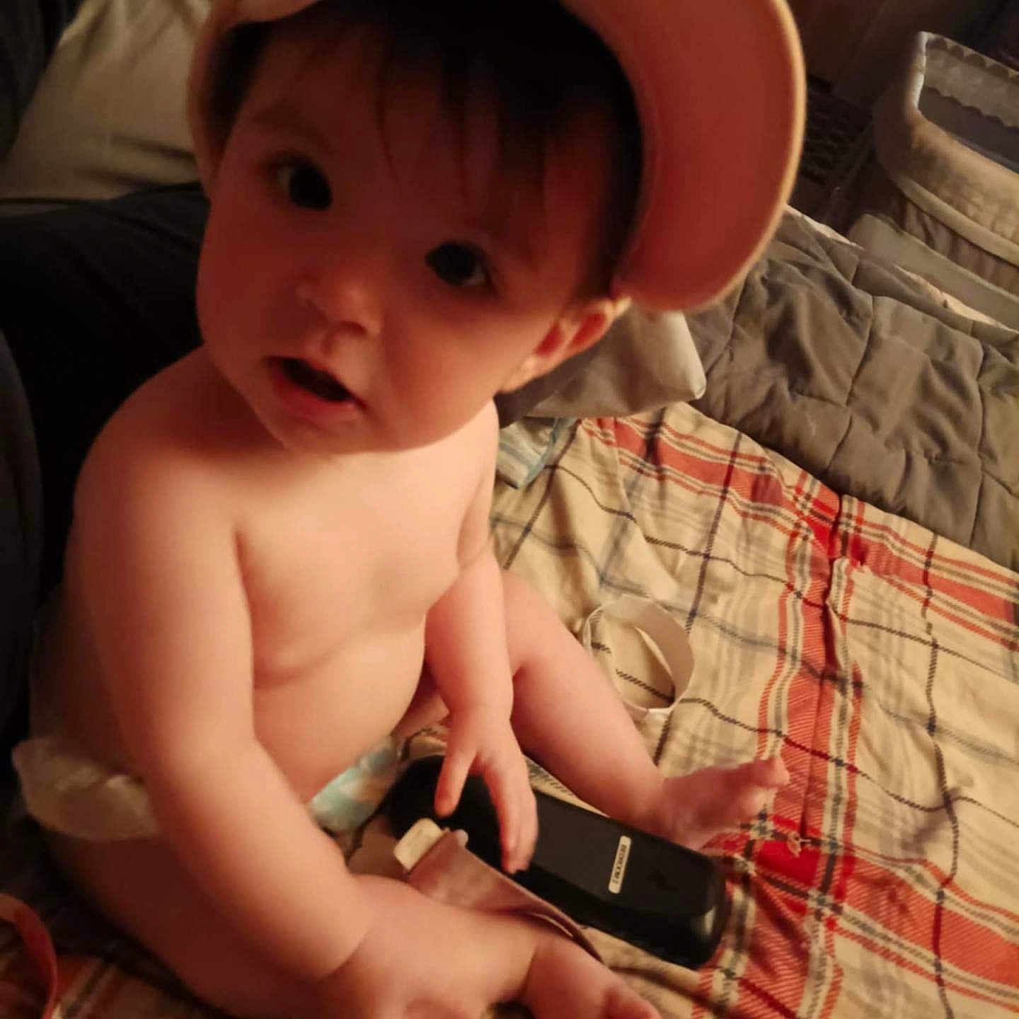 Landry is registered to the contest to win money with this photo: baby, baseballcap, bed, bedroom, bodypart, cap, clothing, electronics, face, finger, furniture, hat, head, indoors, mobilephone, person, phone, photography, portrait, room