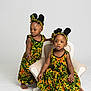afro_hairstyle, armchair, barefoot, child, colorful_clothing, cute, dress, fashion, headband, indoor, matching_outfits, photography, portrait, sitting, standing, studio, toddler, two_children, white_background, young_girls