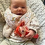 baby, child, infant, smiling, bib, plush_toy, blanket, clothing, floral, cute, soft_texture, hand, face, person, indoors, cozy, pastel_colors, happy, sitting, portrait