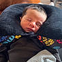 newborn, baby, sleeping, pillow, blanket, clothing, face, infant, rest, comfort, indoor, portrait, person, head, peaceful, cozy, striped_blanket, black_shirt, wood_floor, furniture