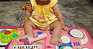 Miracle is registered to the contest to win money with this photo: baby, carpet, child, cute, expression, face, floor, funny, indoor, infant, musical_toys, play_mat, pout, sitting, smiling, toy_drums, toy_keyboard, toy_maracas, toy_microphone, yellow_dress