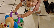 Miracle is registered to the contest to win money with this photo: baby, walker, toy, adult, dog, floor, tile, support, smile, child, indoor, play, learning, cute, person, footwear, jeans, earring, necklace, hand