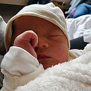Enéa participe au concours pour gagner de l'argent avec cette photo : newborn, baby, infant, sleeping, white_blanket, white_hat, hand, fist, face, cozy, indoor, person, blurred_background, soft_light, clothing, resting, cute, peaceful, child, portrait