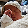 newborn, baby, infant, sleeping, white_blanket, white_hat, hand, fist, face, cozy, indoor, person, blurred_background, soft_light, clothing, resting, cute, peaceful, child, portrait