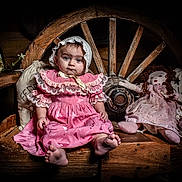 Alessia Reign is registered to the contest to win money with this photo: baby, child, pink_dress, bonnet, wooden_bench, wagon_wheel, rag_doll, flowers, vintage_style, portrait, indoor, cute, sitting, decor, wood, person, soft_lighting, face, feet, fabric