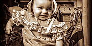 Alessia Reign is registered to the contest to win money with this photo: baby, bonnet, child, clothing, coat, cute, dress, furniture, hand, hanger, happy, holding, indoor, person, portrait, room, sepia, shelf, smile, vintage