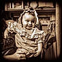 Alessia Reign is registered to the contest to win money with this photo: baby, child, smile, dress, bonnet, hand, person, clothing, indoor, vintage, sepia, furniture, shelf, coat, hanger, portrait, cute, happy, holding, room