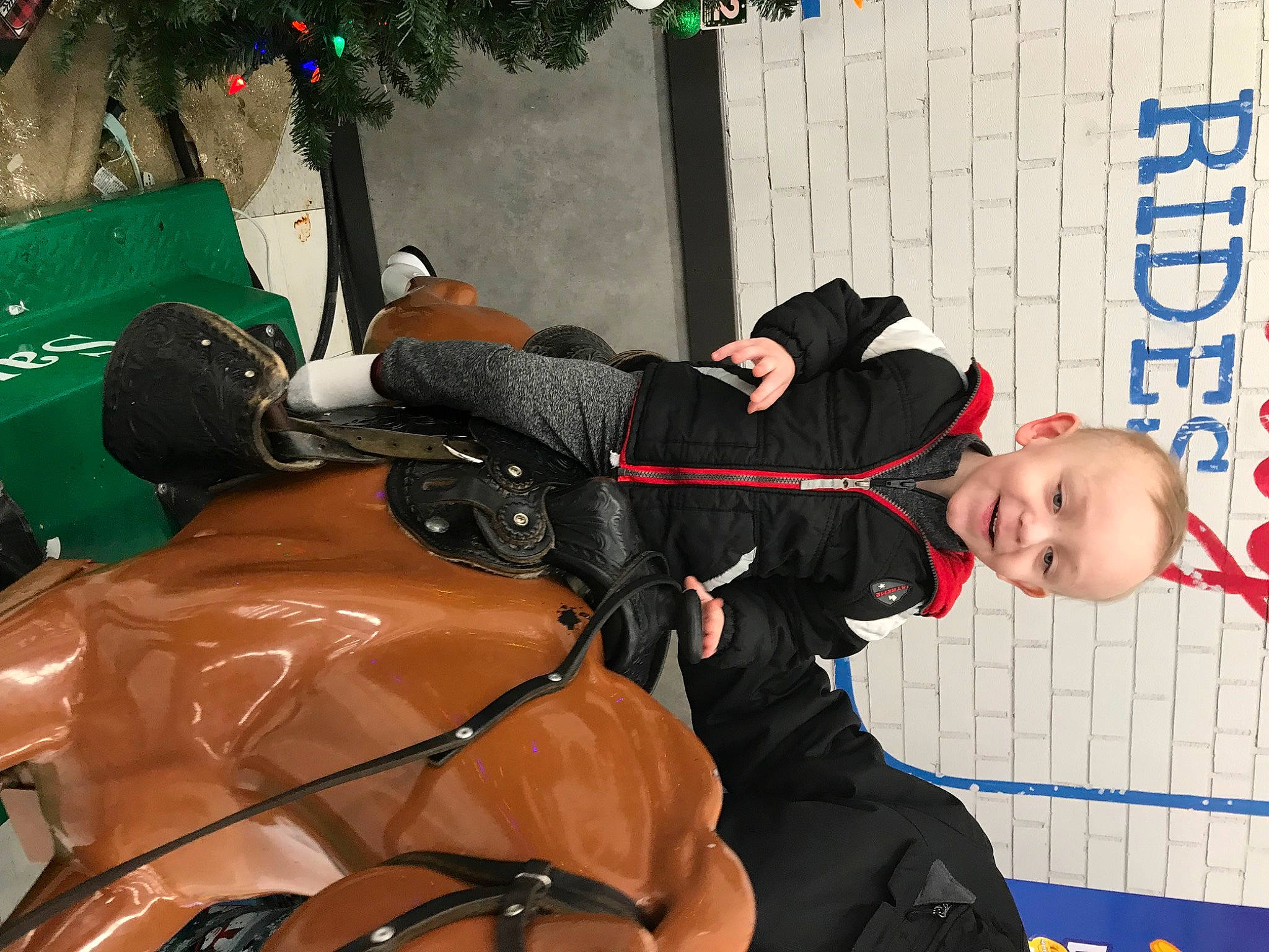 Joseph Jr is registered to the contest to win money with this photo: boot, bridle, christmas_tree, event, glove, hat, holiday, horse, horse_tack, jacket, joy, person, personal_protective_equipment, recreation, rein, smile, toddler, tree, window, winter