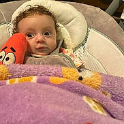 Wynter joined the competition — help win amazing prizes! baby, infant, blanket, plush_toy, chair, curly_hair, indoors, wide_eyes, face, cozy, child, soft_toy, purple_blanket, cute, seated, expression, closeup, comfort, person, looking_away