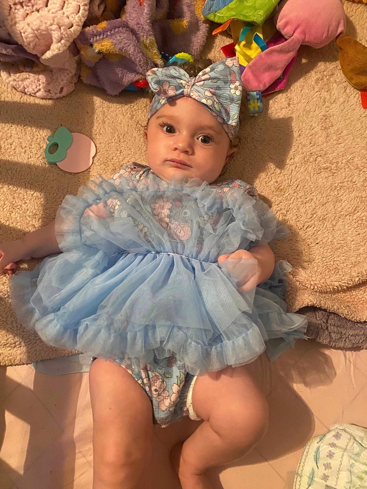 Wynter is registered to the contest to win money with this photo: baby, infant, blue_dress, headband, blanket, soft_toys, lying_down, curious_expression, indoors, plush, child, cute, cozy, fabric, cloth, person, toddler, wearing, portrait, resting