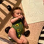baby, infant, avocado, onesie, crib, blanket, milestone, age_sign, handwritten_sign, cuddly, cute, smiling_face, food, fruit, playful, soft_texture, indoor, child, person, lying_down